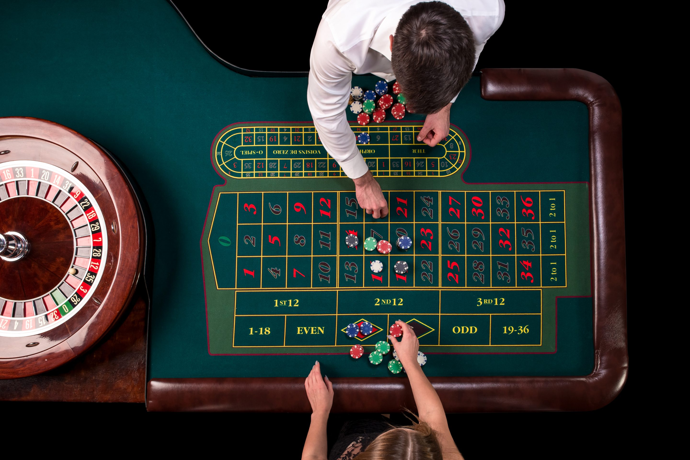 Vista aérea de una mesa de juego en el casino, se ve a una mujer croupier dando fichas y a un hombre jugando mientras las coloca; imagen para ilustrar el artículo de profesiones poco conocidas en España, en este caso la profesión de fisionomista de casinos.