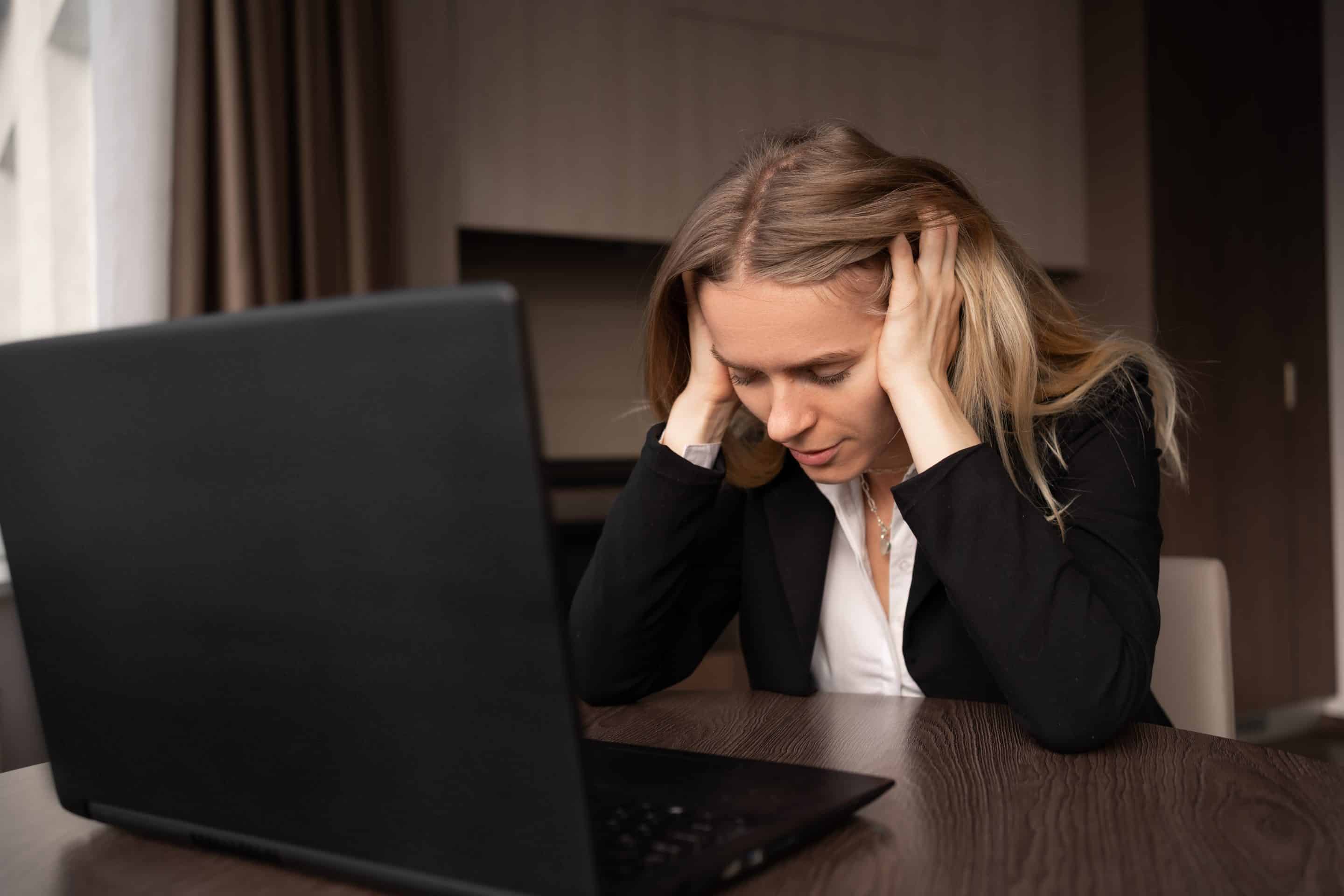 Una mujer sentada en su puesto de trabajo con las manos en la cabeza muestra signos de estrés y parece agobiada